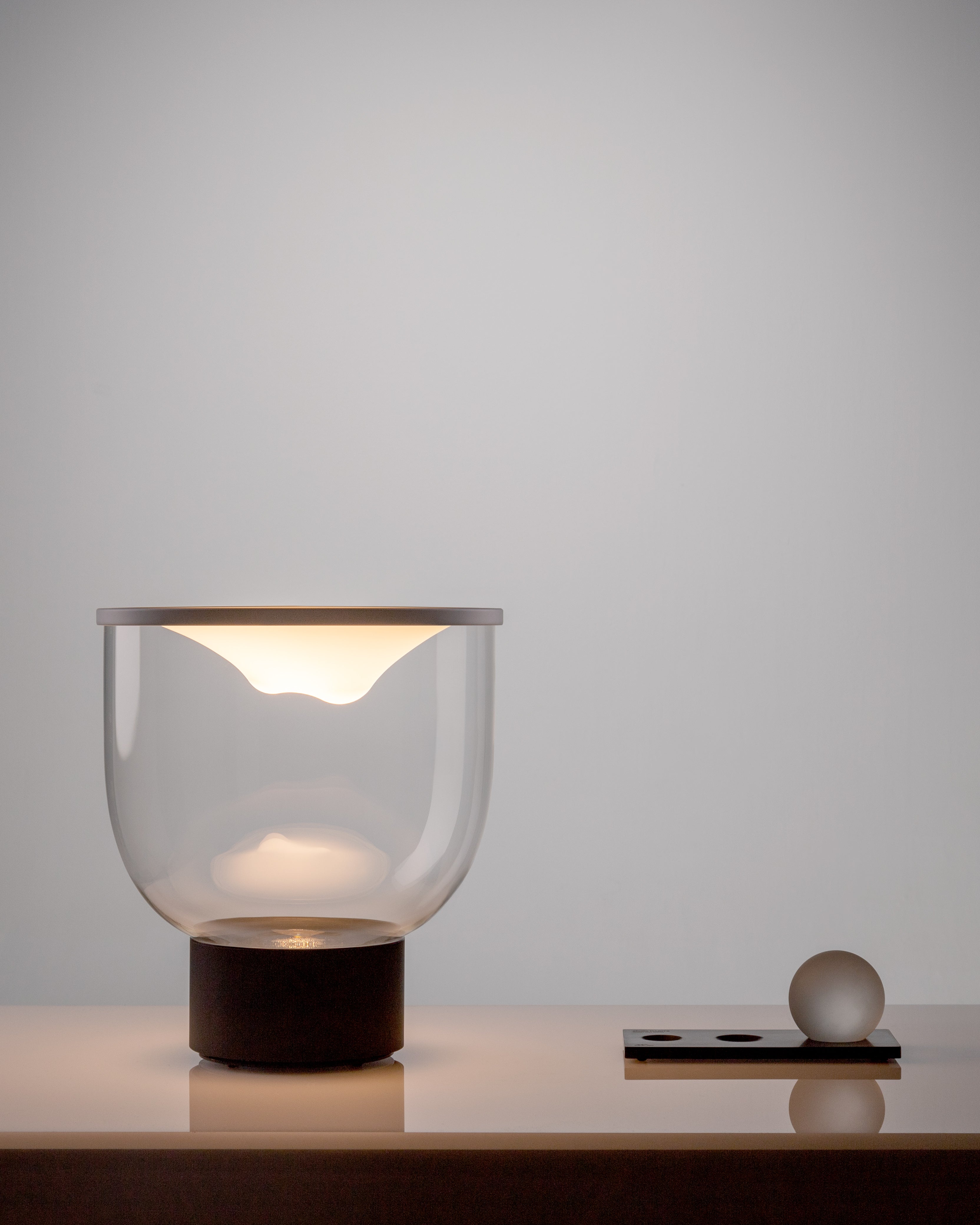 Stolní lampa GRAMMOLUCE se skleněným stínidlem a černým podstavcem.