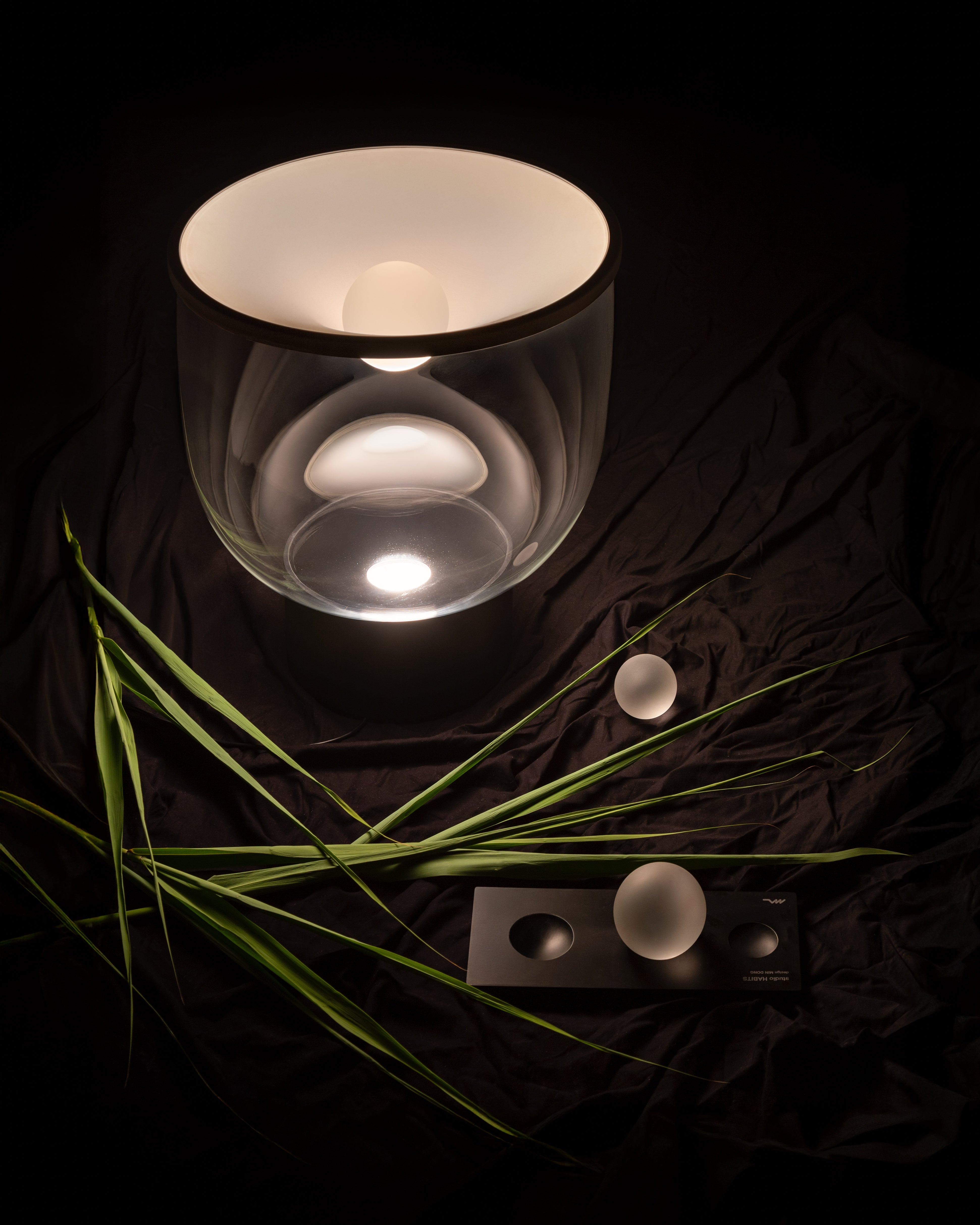 Stolní lampa GRAMMOLUCE se skleněným stínidlem a černým podstavcem.